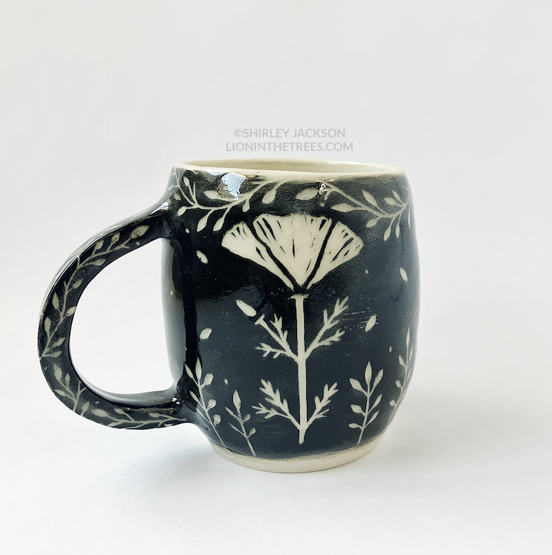 Photo of my black sgraffito mug. Shoes the back of the mug that has a poppy flower motif