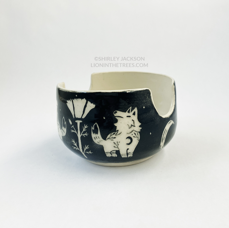 Photo of my black sgraffito brush holder bowl featuring my Keeper Wolves motif and a poppy