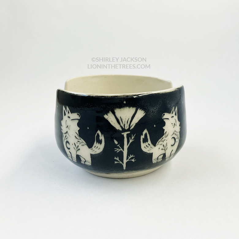 Photo of my black sgraffito brush holder bowl featuring my Keeper Wolves motif and a poppy