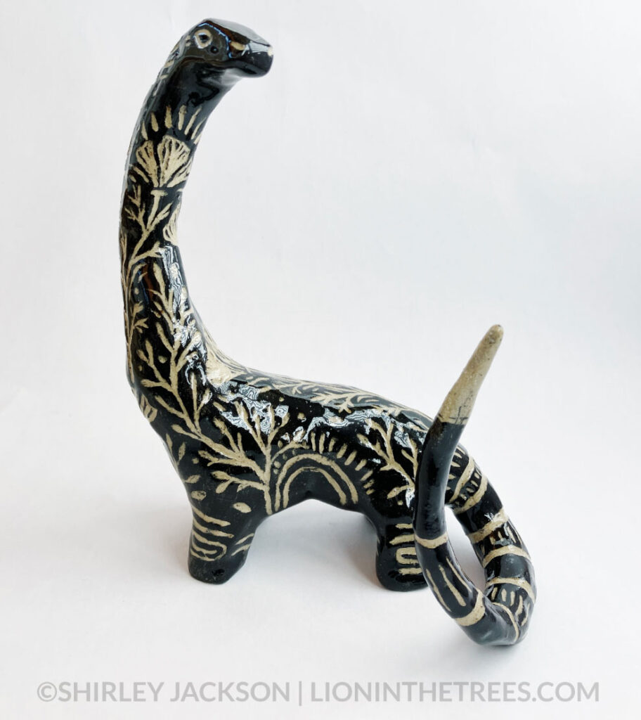 A brontosaur sculpture done in a black with sgraffito details.