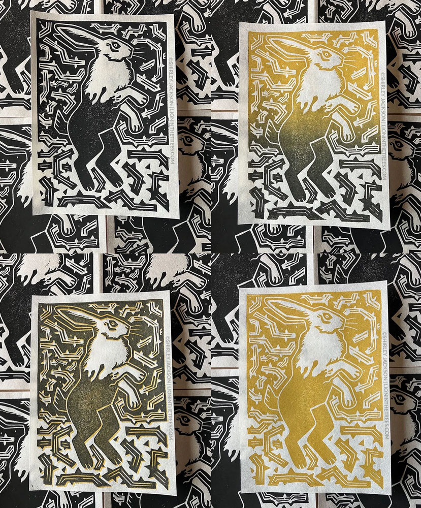 A photo of four linoblock prints featuring a rabbit with half it's body covered in black ink surrounded by a bunch of thorns. Going clockwise, the colour variants are:

All black;
Gold to black split fountain roll;
All gold;
Black with an underlying print of gold.