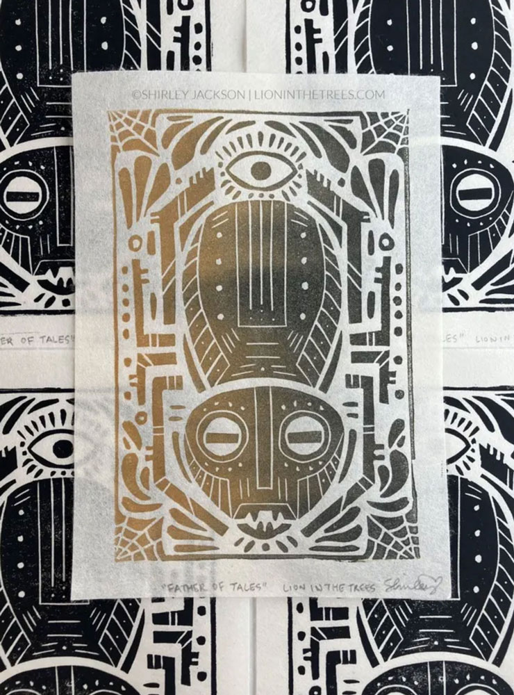 A linoblock print featuring a man spider motif with a variety of other design details such as webs, an eye, and various shapes. This print is a gold to black horizontal split fountain roll.