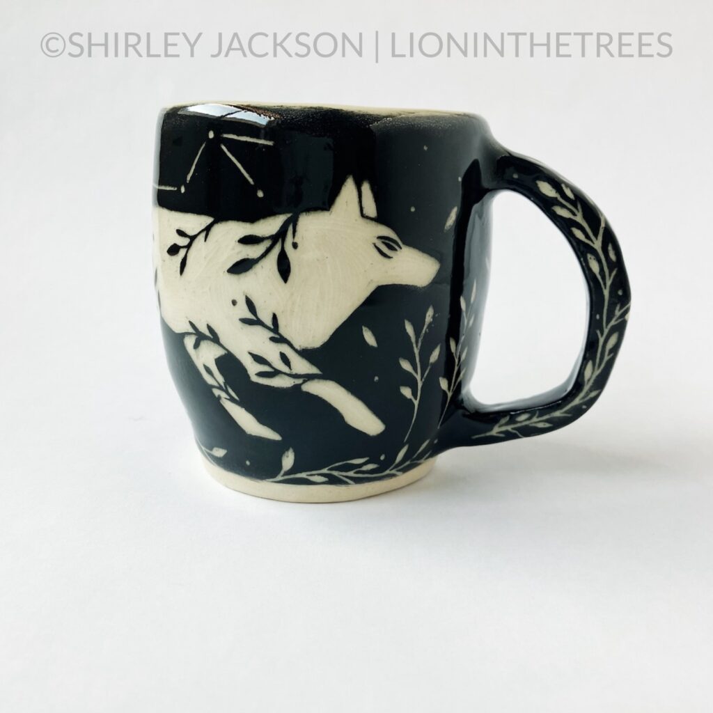 Front View - Ceramic sgraffito mug with black underglaze featuring my running floral wolf motif. Floral details carved into the handle.
