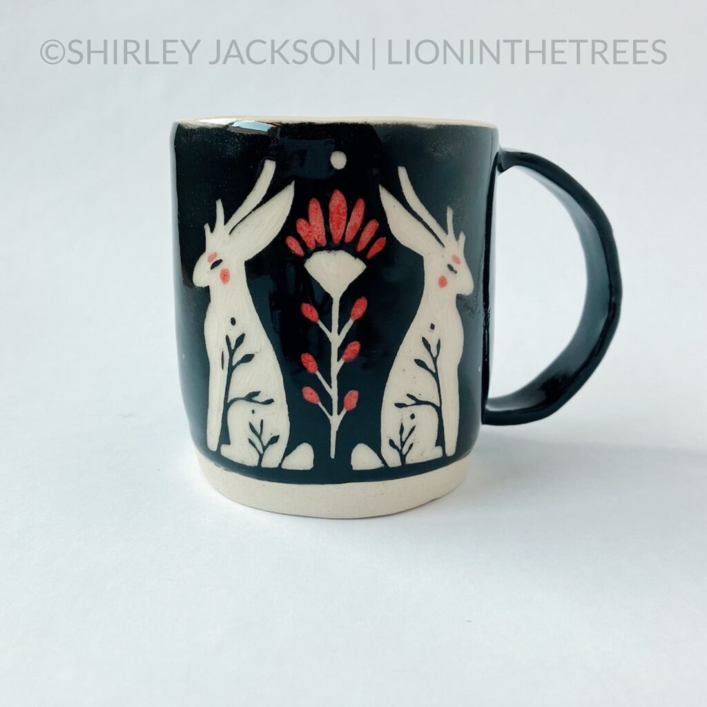 Front View - Ceramic sgraffito mug featuring a pair of Jackalopes and a Prairie Fire flower motif on the front.