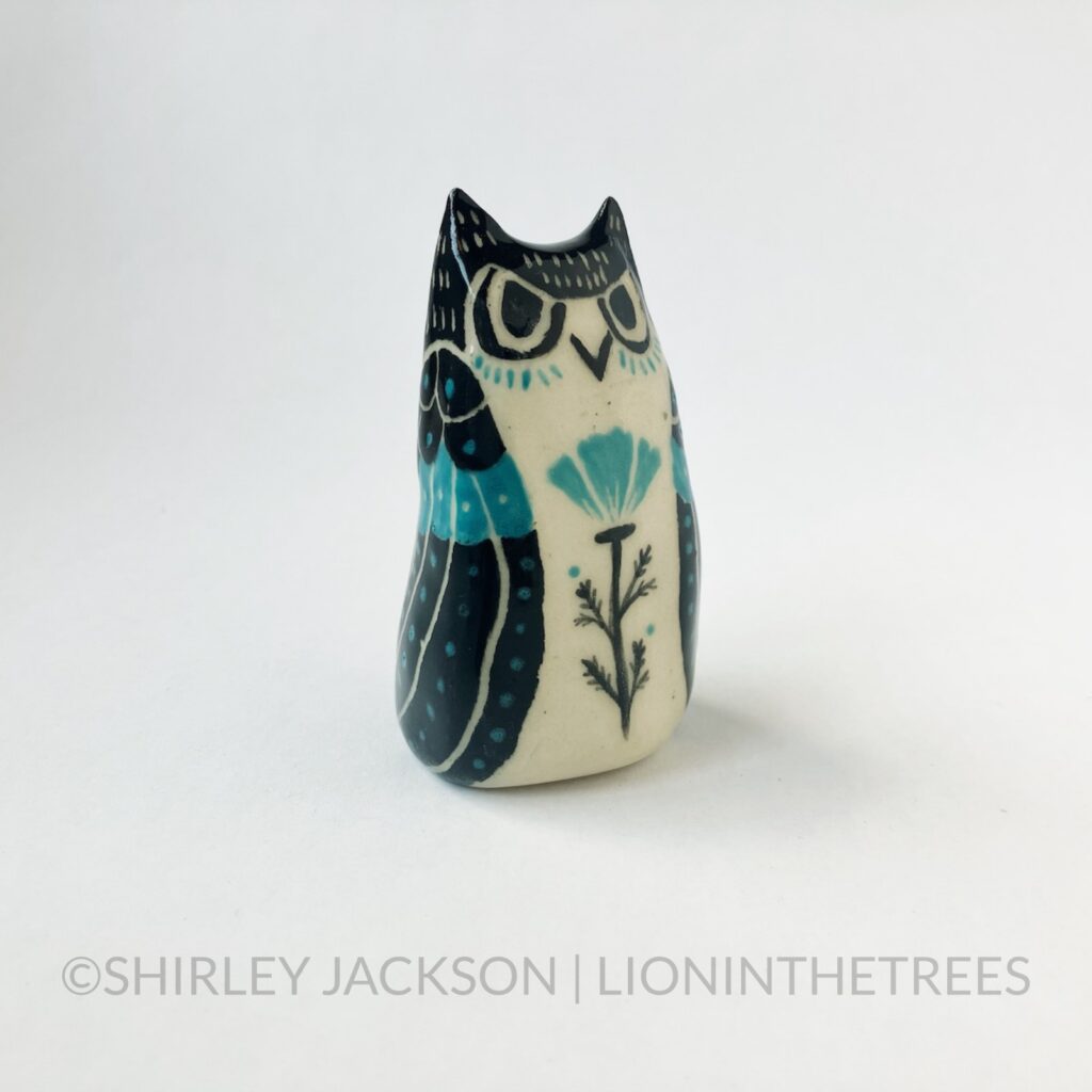 A ceramic sgraffito Horned Owl Totem with black and turquoise underglaze, and a California Poppy on it's front torso.