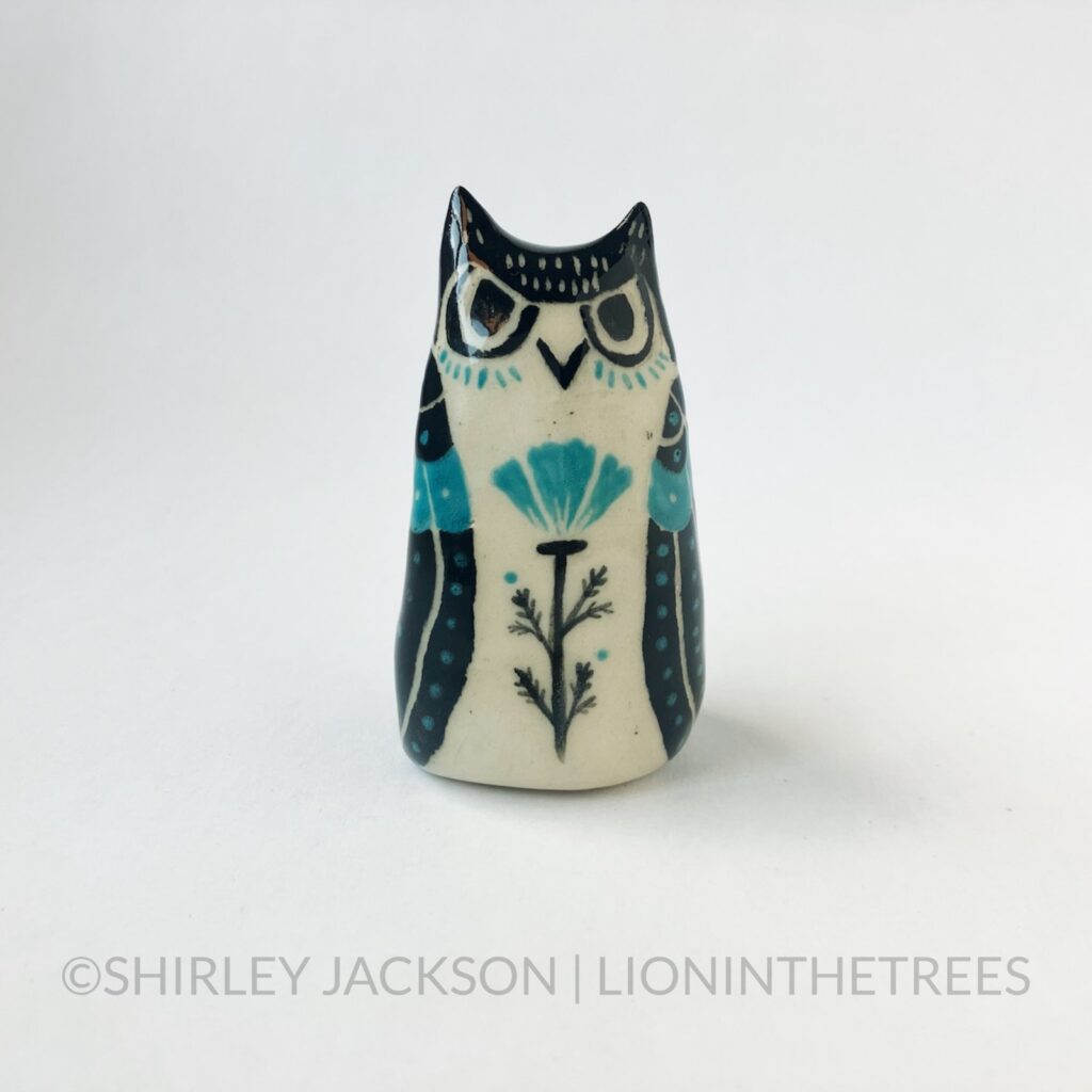 A ceramic sgraffito Horned Owl Totem with black and turquoise underglaze, and a California Poppy on it's front torso.