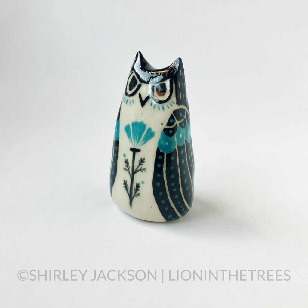 A ceramic sgraffito Horned Owl Totem with black and turquoise underglaze, and a California Poppy on it's front torso.