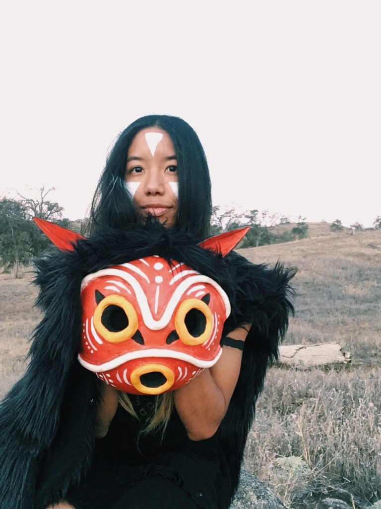 It's me, ya girl, in my DIY San outfit holding up the mask in front of myself with a very happy, content smile on my face.