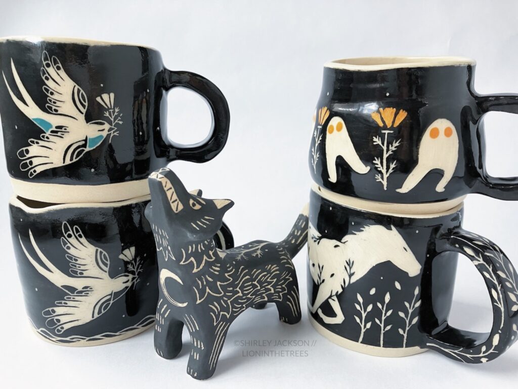 Group photo of my latest pottery. Features a variety mugs with black sgraffito designs consisting of my swallow, Fresno Nightcrawler, and Running Horse motifs. There is also my Howling Wolf totem in the center.