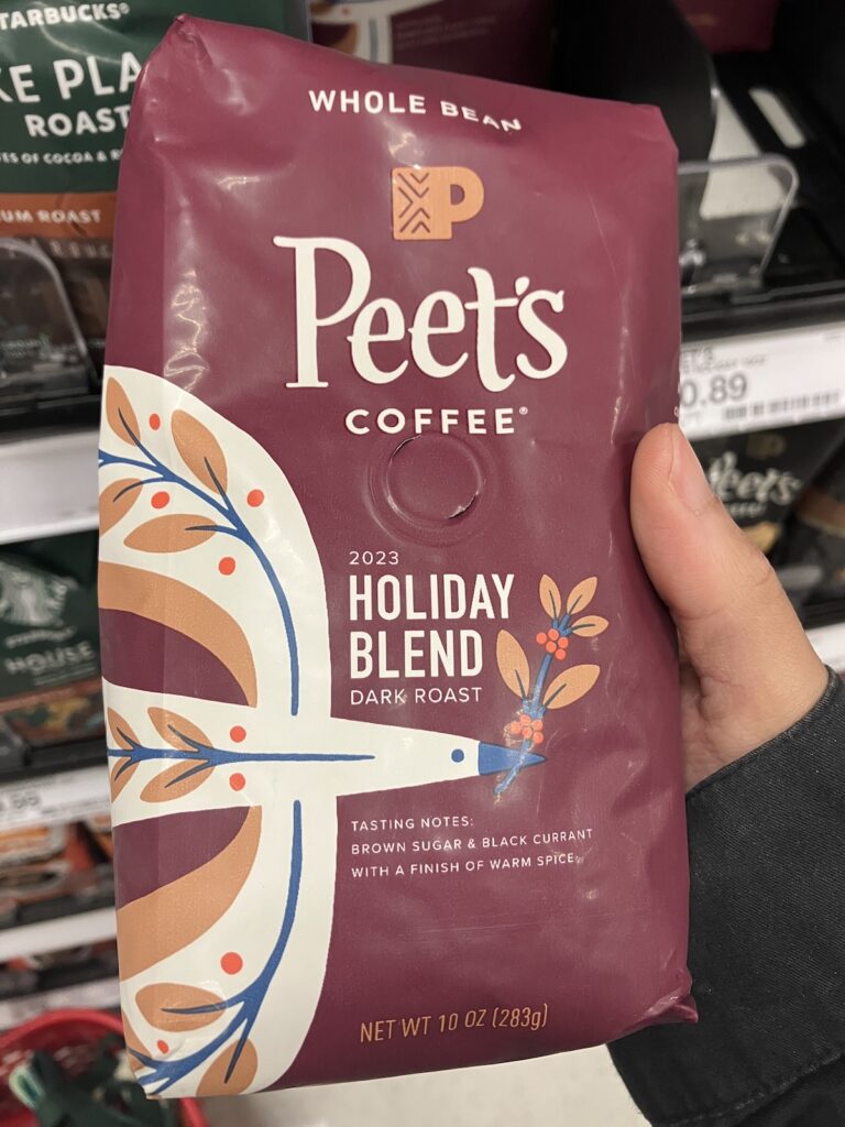 Front packaging of Peet's Coffee Holiday Blend Dark Roast Whole Bean coffee. The bag itself is a nice maroon with a cream coloured, stylistic bird that has floral details on it's body and a sprig in it's beak.