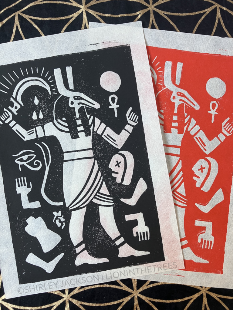 Photo of two block prints of the same image depicting the Egyptian god Set. He is standing with a weapon in one hand, and is surrounded by Osiris' body parts as well as Horus' eye. One print was printed in black and the other in red.