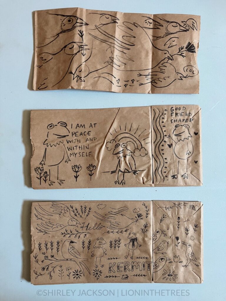 A photo of 3 brown paper lunch bags with a variety of doodles drawn with a sharpie and pen on them. This variety features subject matter ranging from Barn Swallow motifs and Kermit the Frog announcing that they are "at peace with and within myself".