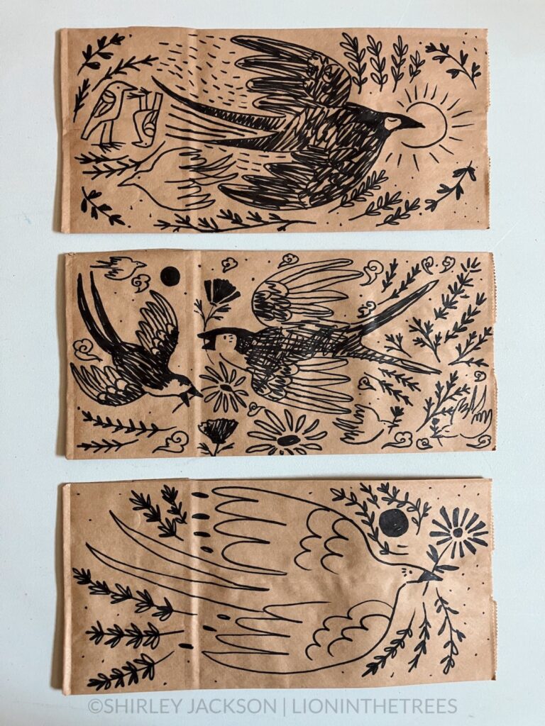 A photo of 3 brown paper lunch bags with a variety of doodles drawn with a sharpie on them. This variety features different Barn Swallow motifs.