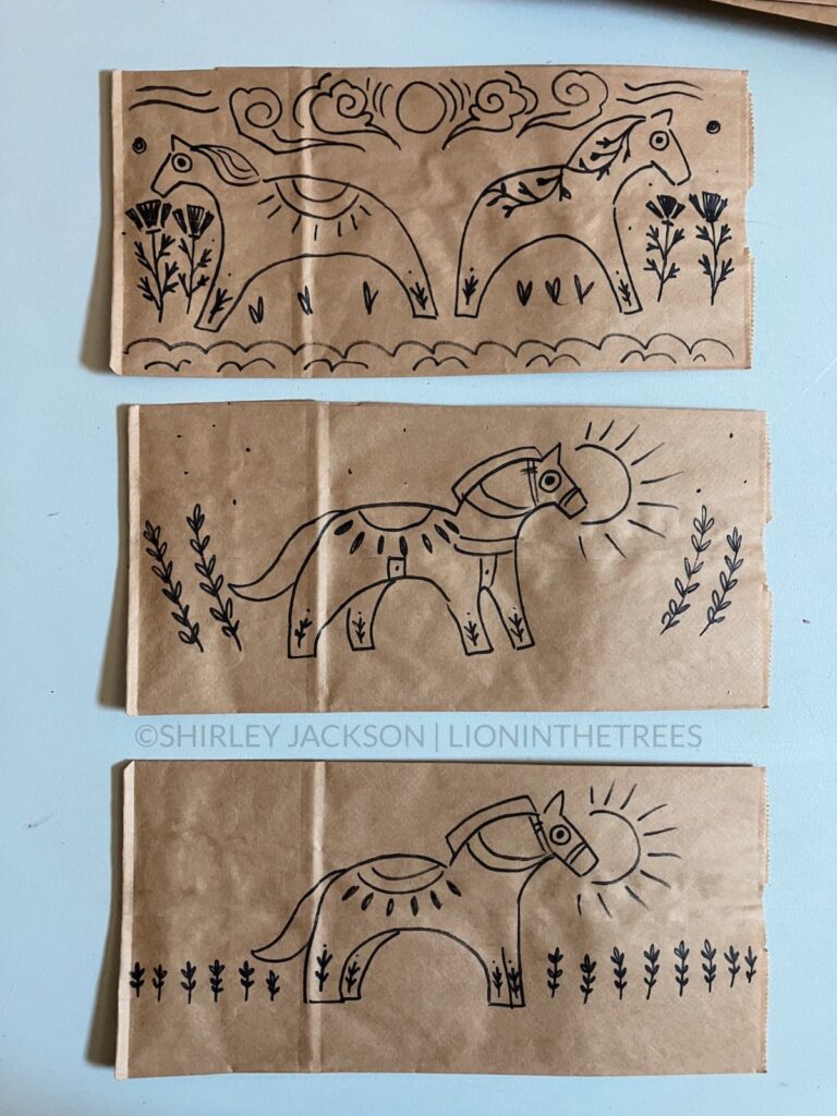 A photo of 3 brown paper lunch bags with a variety of doodles drawn with a sharpie on them. This variety features Dala Horses