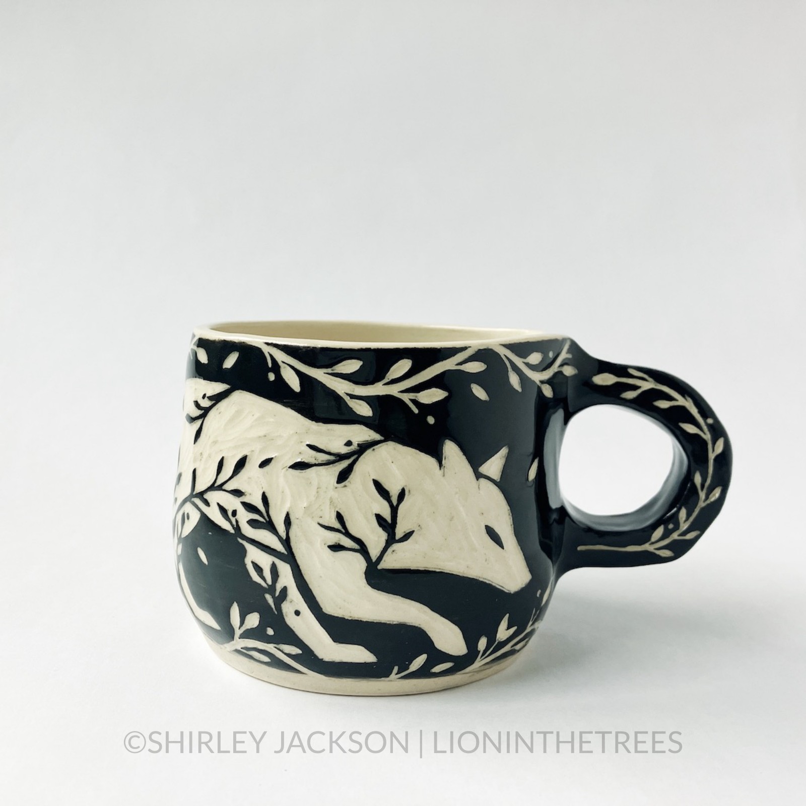 Ceramic black sgraffito mug featuring my Running Fox motif. This mug also features a floral border above and below the fox motif.