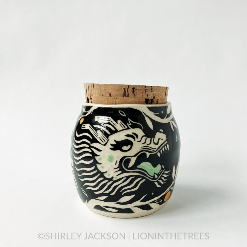 Dragon memory jar with a cork lid featuring my sgraffito dragon motif. This one was done with black and pistachio green underglaze surrounded by tree branches and oranges.