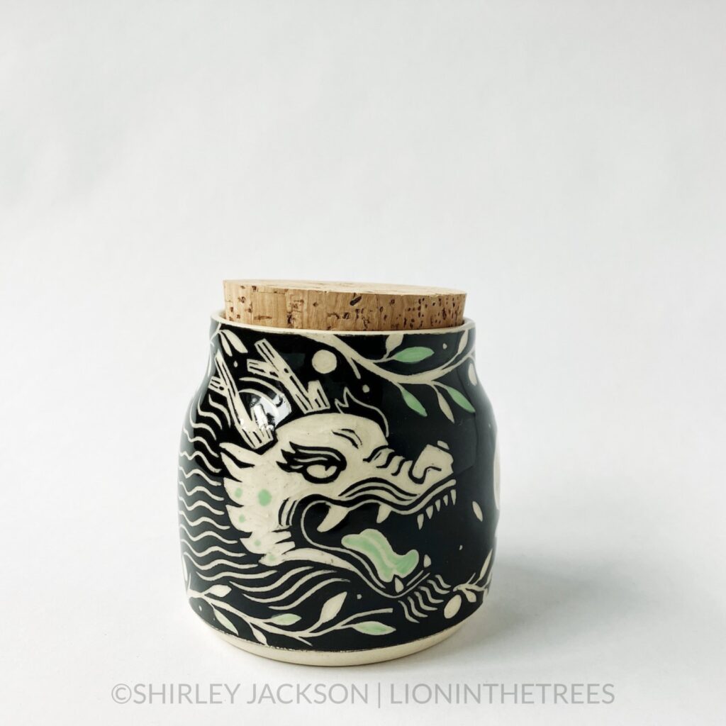 Dragon memory jar with a cork lid featuring my sgraffito dragon motif. This one was done with black and pistachio green underglaze surrounded by tree branches.