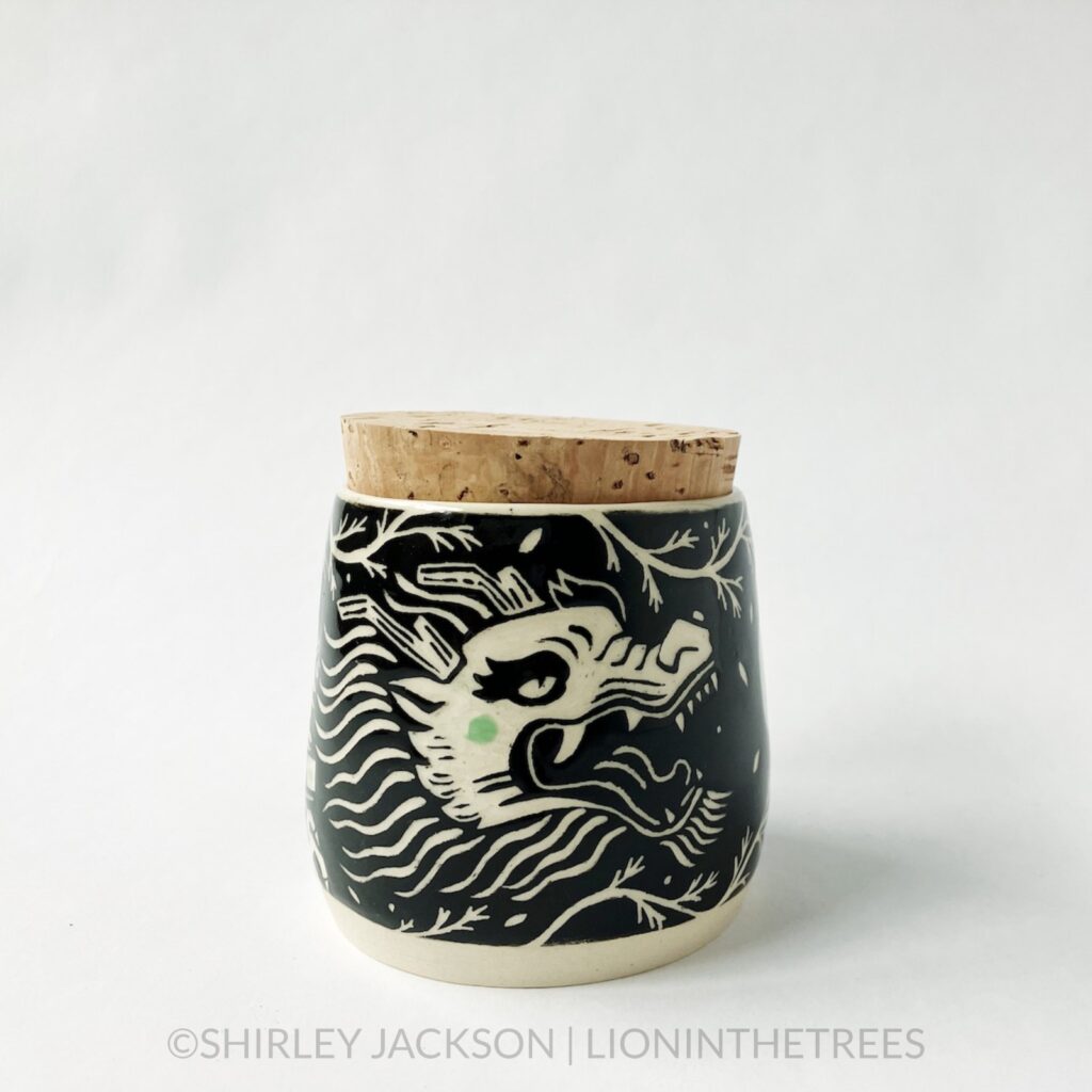 Dragon memory jar with a cork lid featuring my sgraffito dragon motif. This one was done with black and pistachio green underglaze surrounded by California Poppy stems.