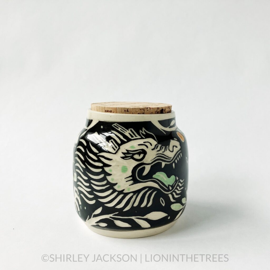 Dragon memory jar with a cork lid featuring my sgraffito dragon motif. This one was done with black and pistachio green underglaze surrounded by tree branches, and oranges.
