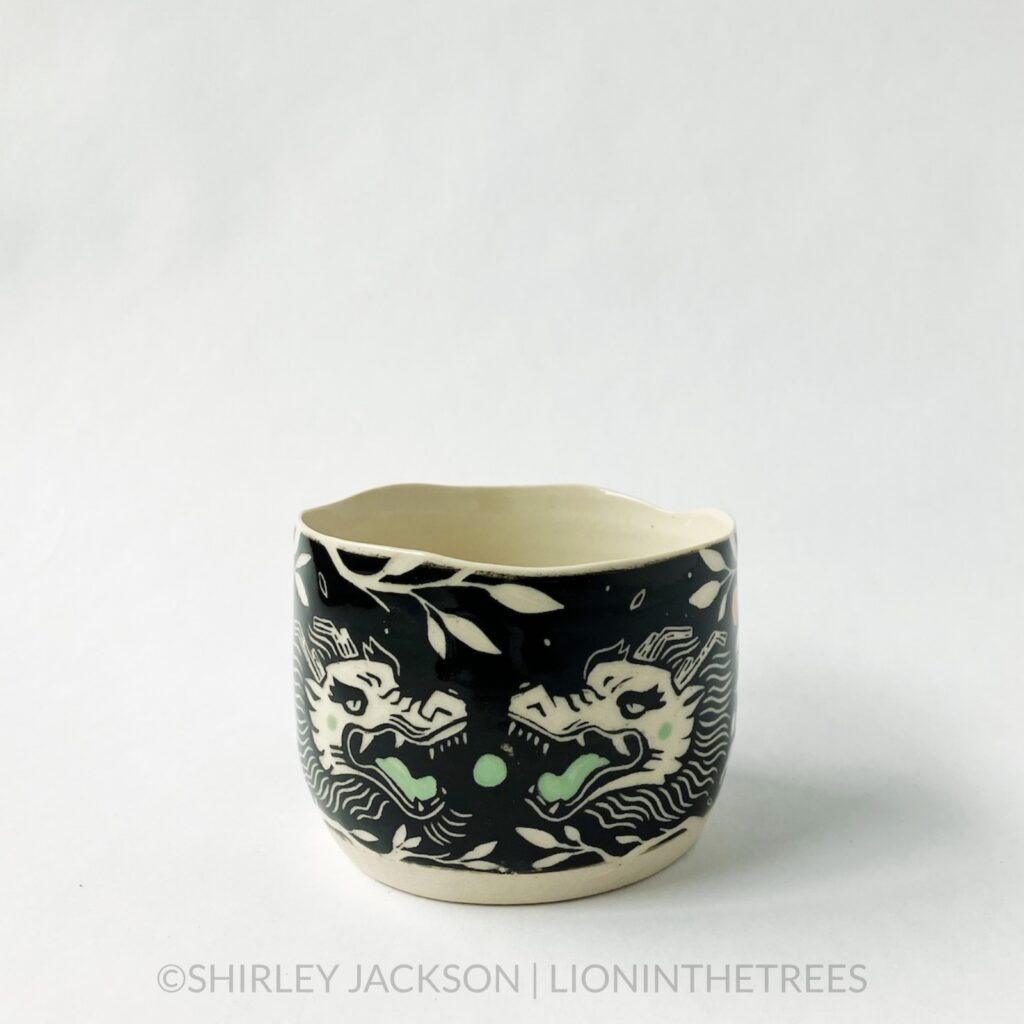 Dragon bowl featuring twins of my sgraffito dragon motif. This one was done with black and pistachio green underglaze, tree branches, and oranges. This photo shows the front of the bowl where the two dragon heads meet as though they're about to bite the green orb in the center.