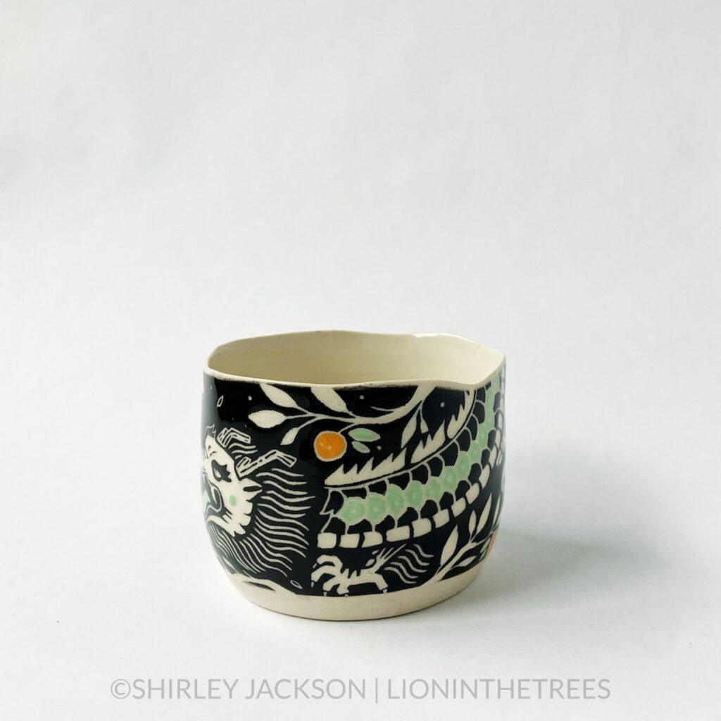 Dragon bowl featuring twins of my sgraffito dragon motif. This one was done with black and pistachio green underglaze, tree branches, and oranges. This photo shows the right side of the bowl and one of the dragons.