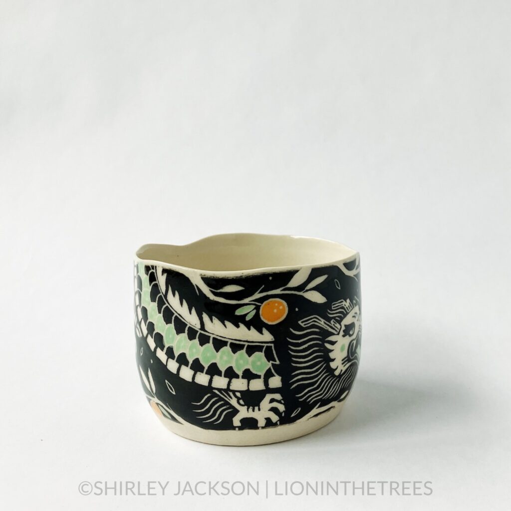 Dragon bowl featuring twins of my sgraffito dragon motif. This one was done with black and pistachio green underglaze, tree branches, and oranges. This photo shows the left side of the bowl and one of the dragons.