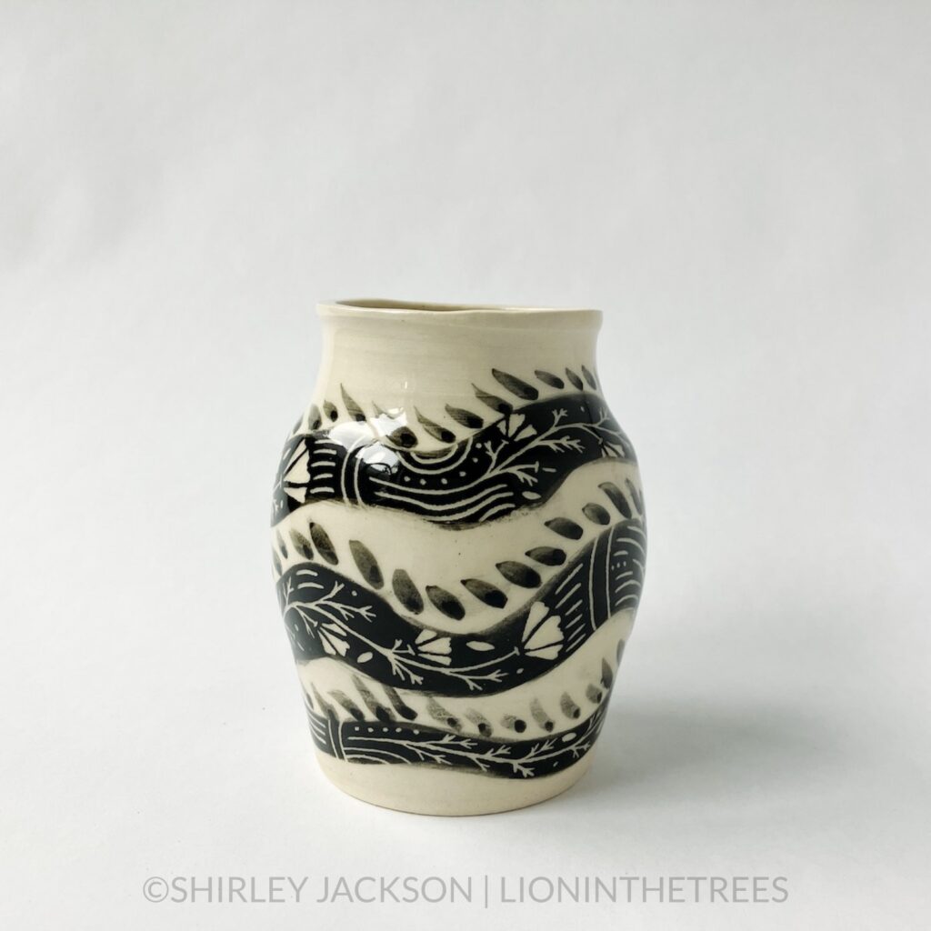 A dragon vase featuring an experimental dragon motif done in black underglaze painted directly onto the creamy white body of the clay. This photo shows a side of the jar as the dragon's body wraps around the circumference of the jar three times.