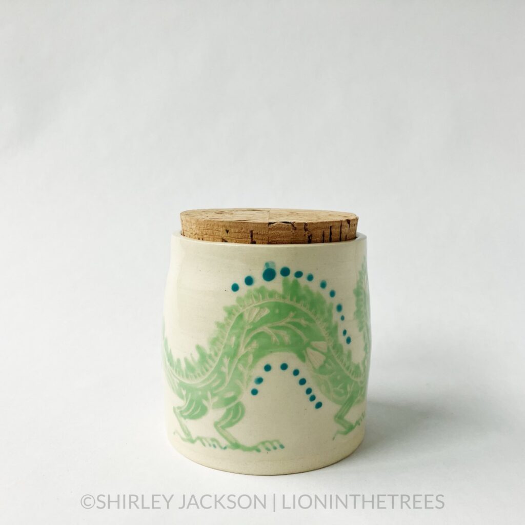 Dragon memory jar with a cork lid featuring an experimental sgraffito dragon motif. This one was done with pistachio green and turquoise underglaze directly painted onto the creamy coloured clay body of the jar.