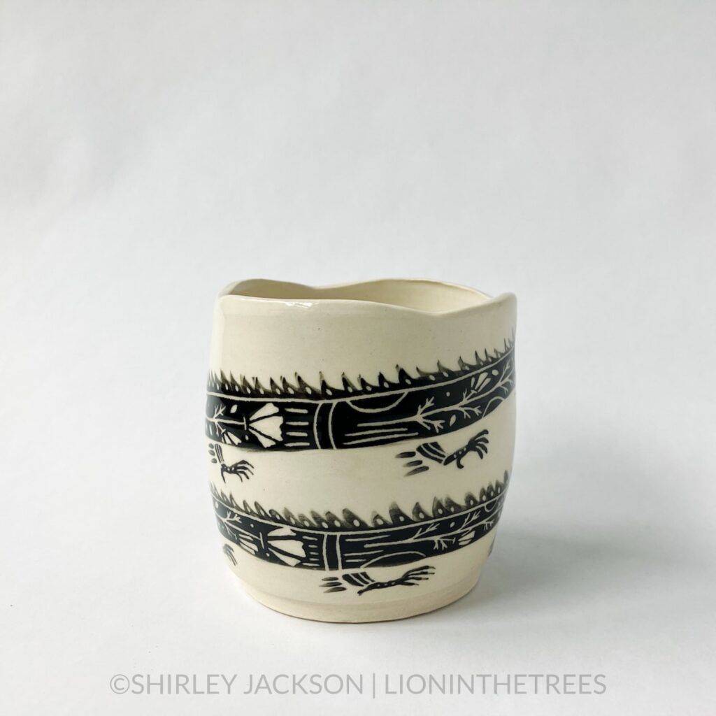 A dragon planter featuring an experimental dragon motif done in black underglaze painted directly onto the creamy white body of the clay. This photo shows a side of the jar showing parts of it's body as it wraps around the circumference of the planter.