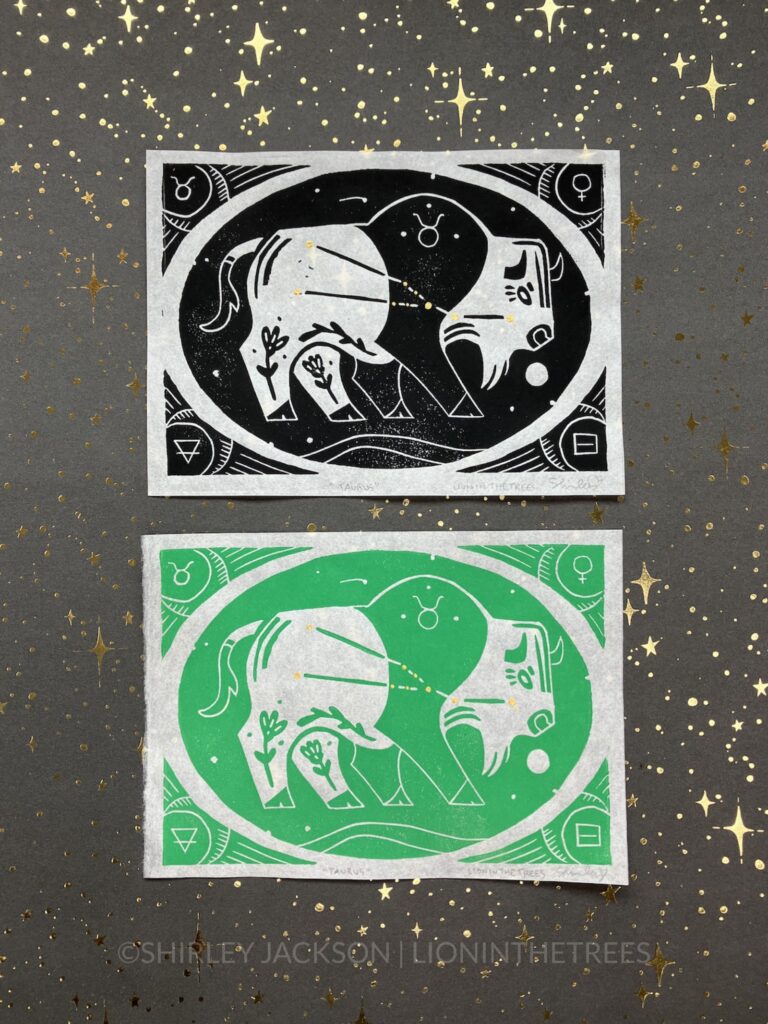 Photo of an all black and an all green block print featuring the astrological sign of Taurus as an American Bison with the constellation hand-painted with gold stars on the bison's body. They are enclosed within an oval that has stars within it, and a border that has symbolic signs that coordinate with Taurus.