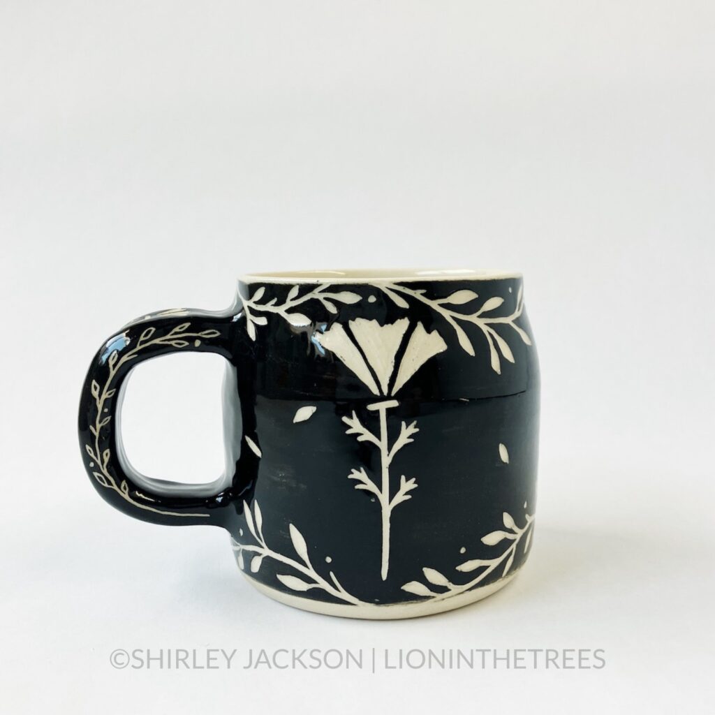 Ceramic black sgraffito mug featuring my Running Bison motif. This mug also features a floral border above and below the Bison motif. This shows the back that features a California Poppy motif.
