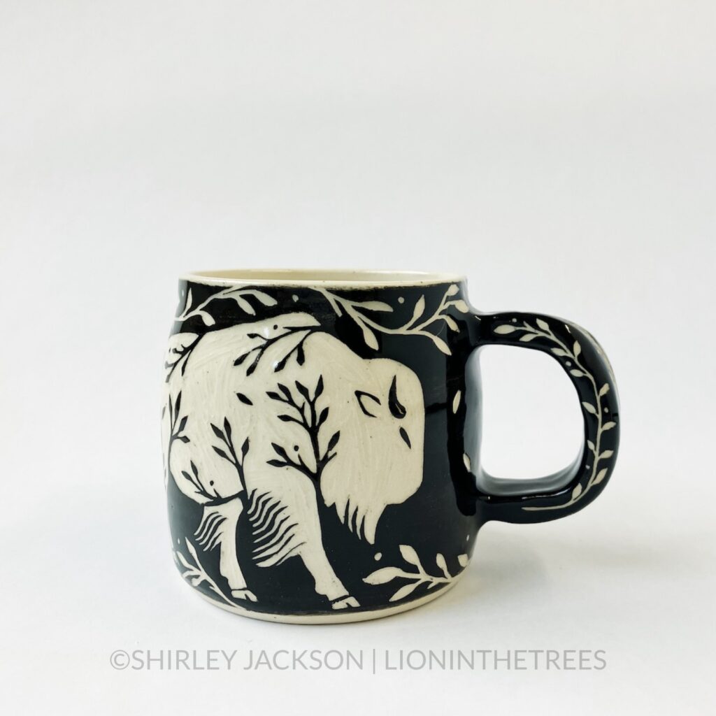 Ceramic black sgraffito mug featuring my Running Bison motif. This mug also features a floral border above and below the Bison motif.