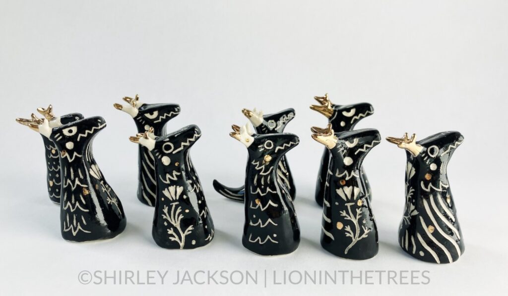 A group of 9 small black sgraffito dragon totems done with touches of gold arranged to face towards the right of the picture frame. They look as though they're shuffling in that direction.