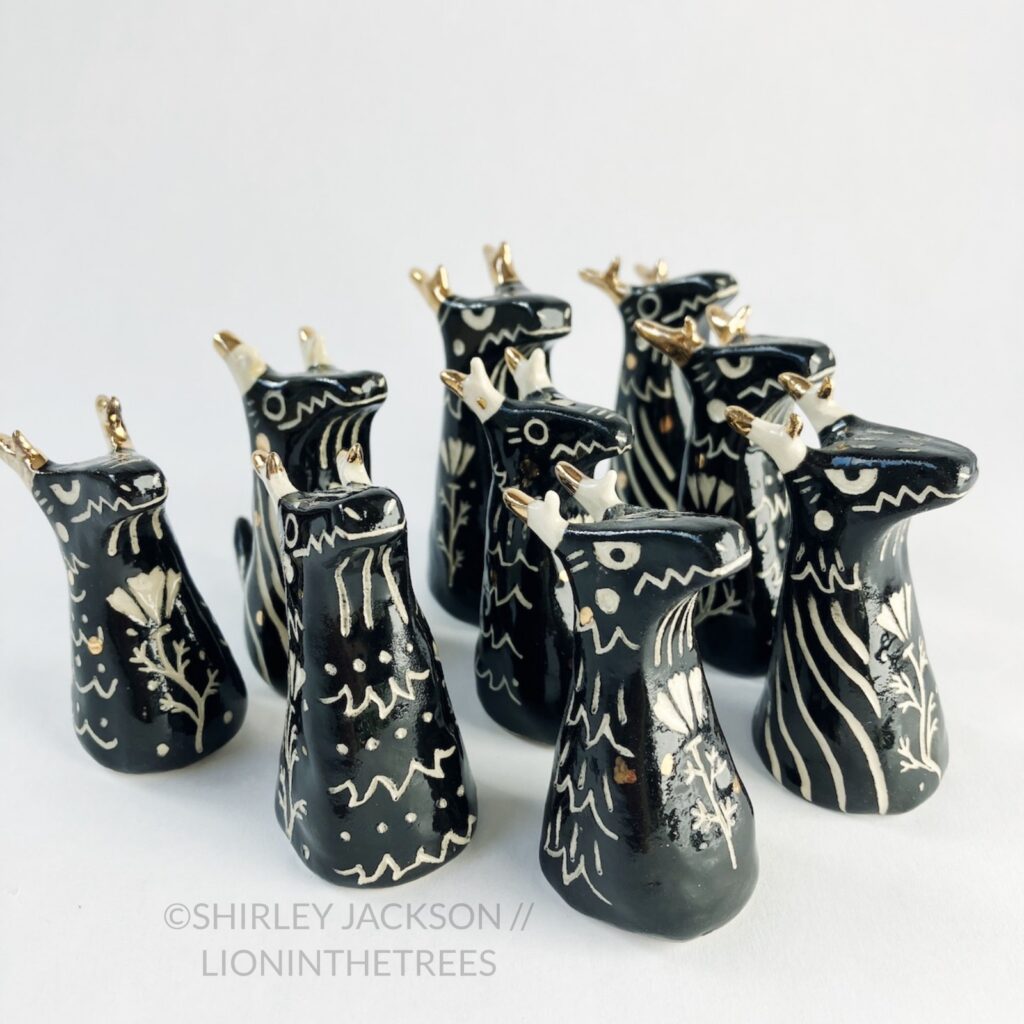 A group of 9 small black sgraffito dragon totems done with touches of gold arranged diagonally.