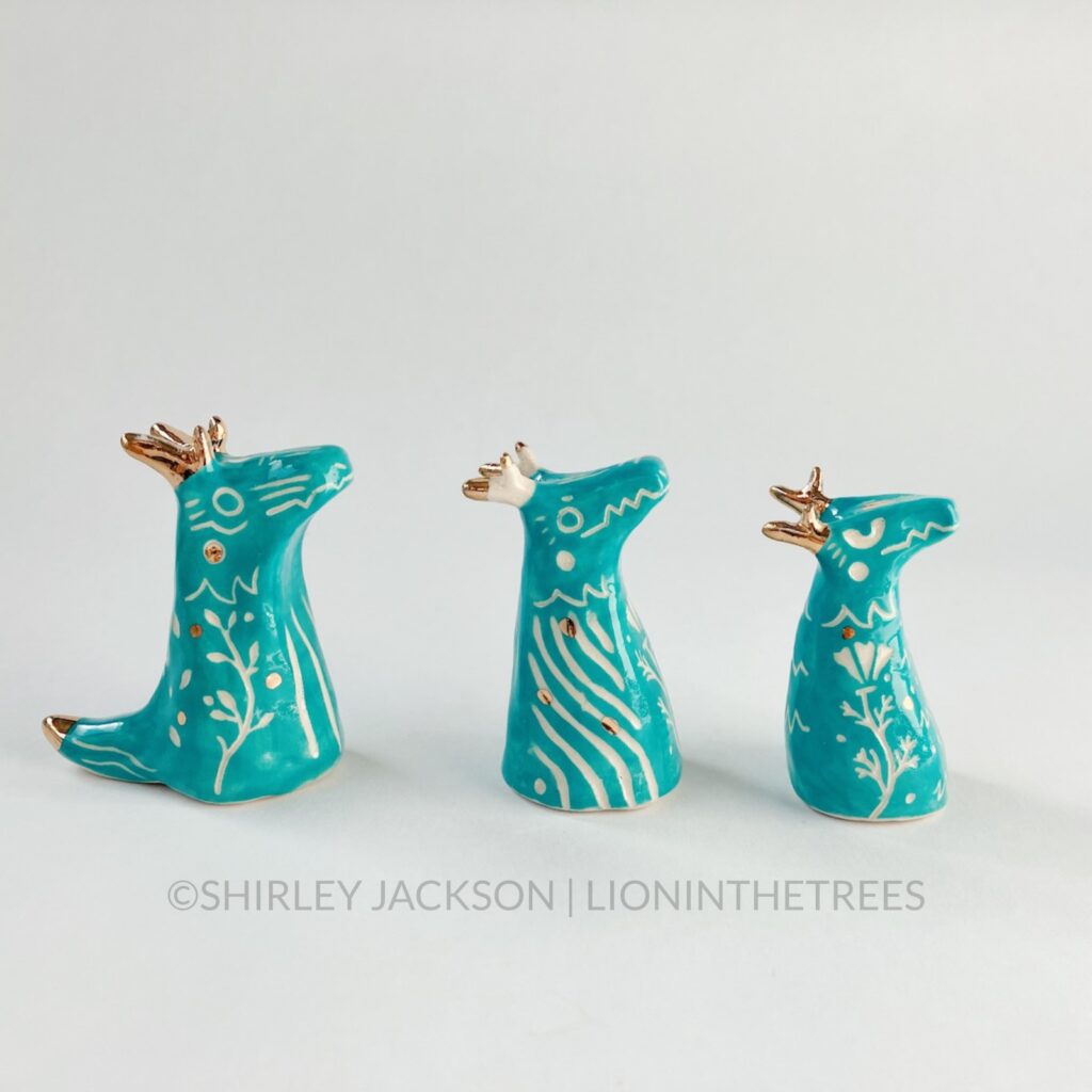 A group of 3 small turquoise sgraffito dragon totems done with touches of gold arranged in a row.