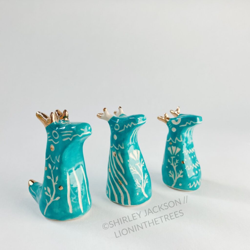 A group of 3 small turquoise sgraffito dragon totems done with touches of gold arranged diagonally.
