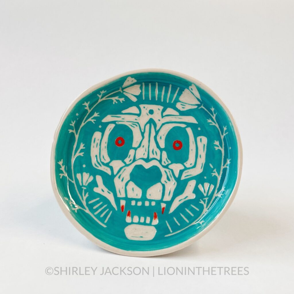 A small, turquoise sgraffito trinket dish with my Devil Dog motif. In this version, the skull dog’s eyes and canine teeth are painted red.
