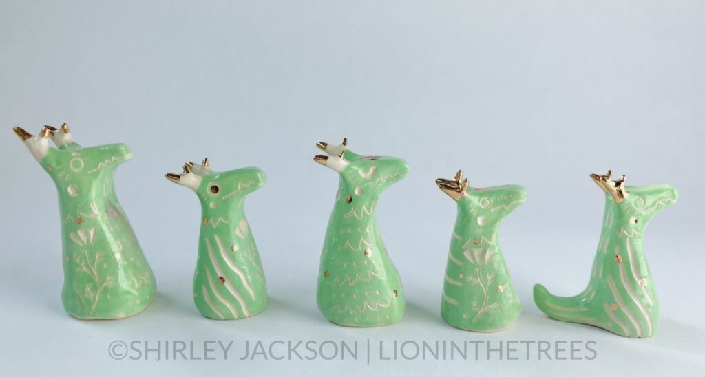 A group of 5 small green sgraffito dragon totems done with touches of gold arranged in a row.