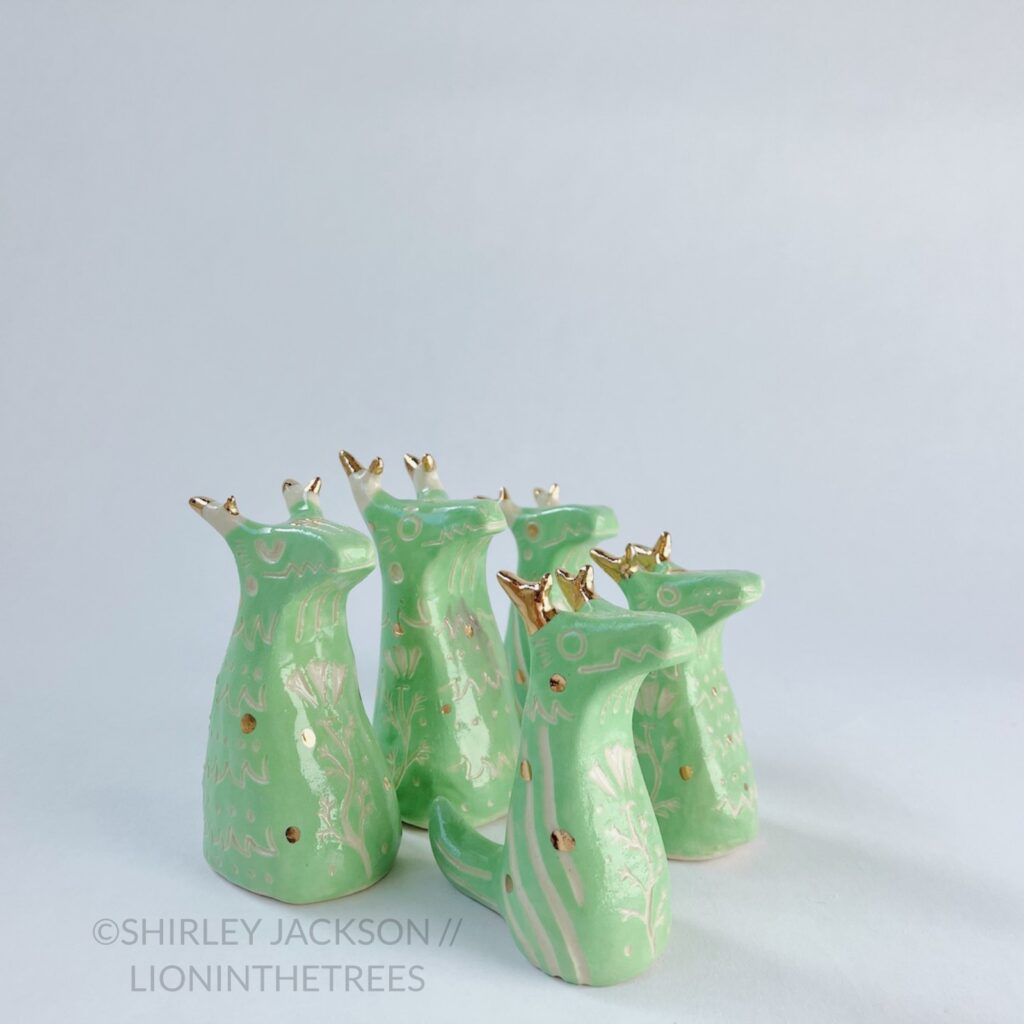 A group of 5 small green sgraffito dragon totems done with touches of gold arranged diagonally.