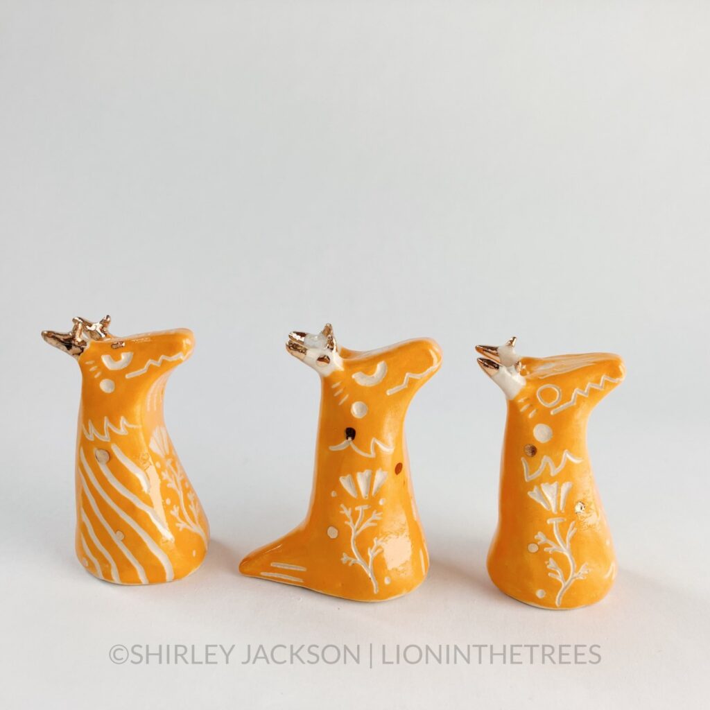 A group of 3 small orange sgraffito dragon totems done with touches of gold arranged in a row.