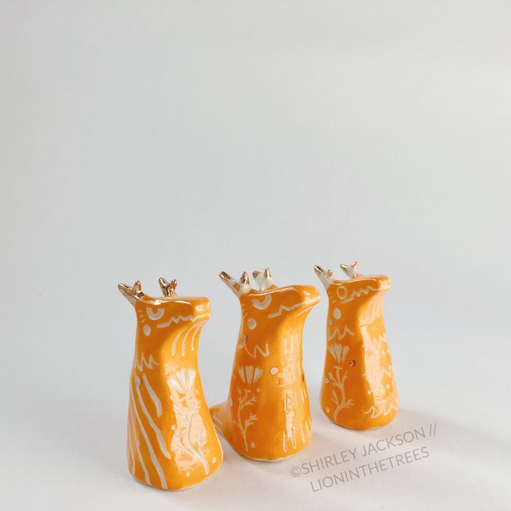 A group of 3 small orange sgraffito dragon totems done with touches of gold arranged diagonally.