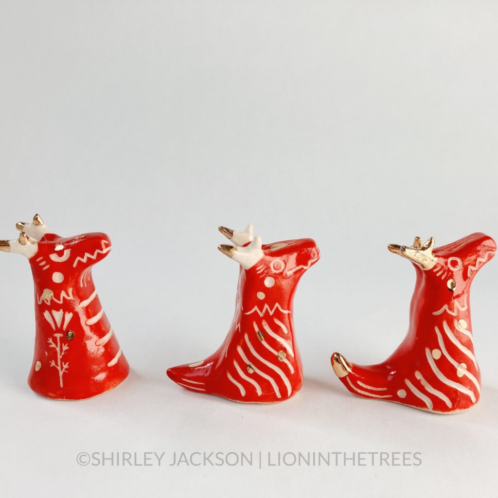 A group of 3 small red sgraffito dragon totems done with touches of gold arranged in a row.