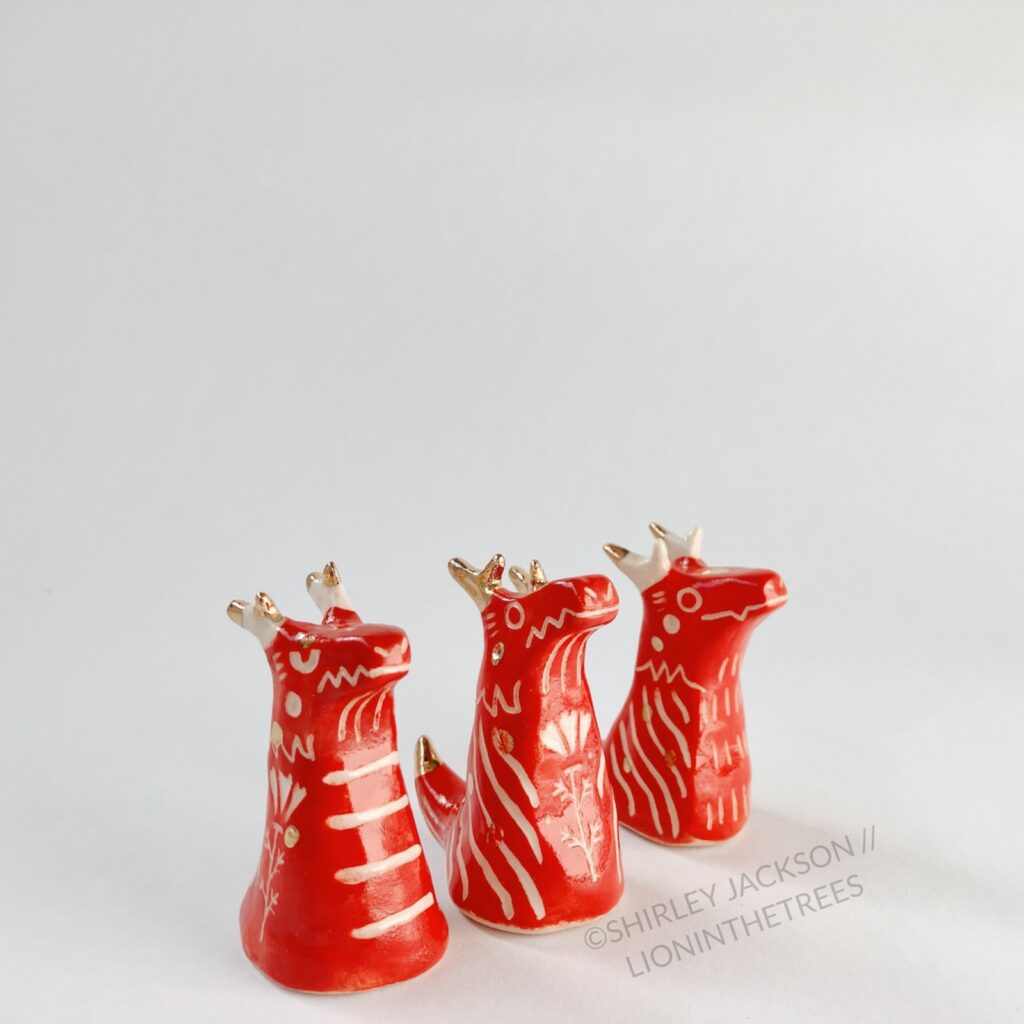 A group of 3 small red sgraffito dragon totems done with touches of gold arranged diagonally.