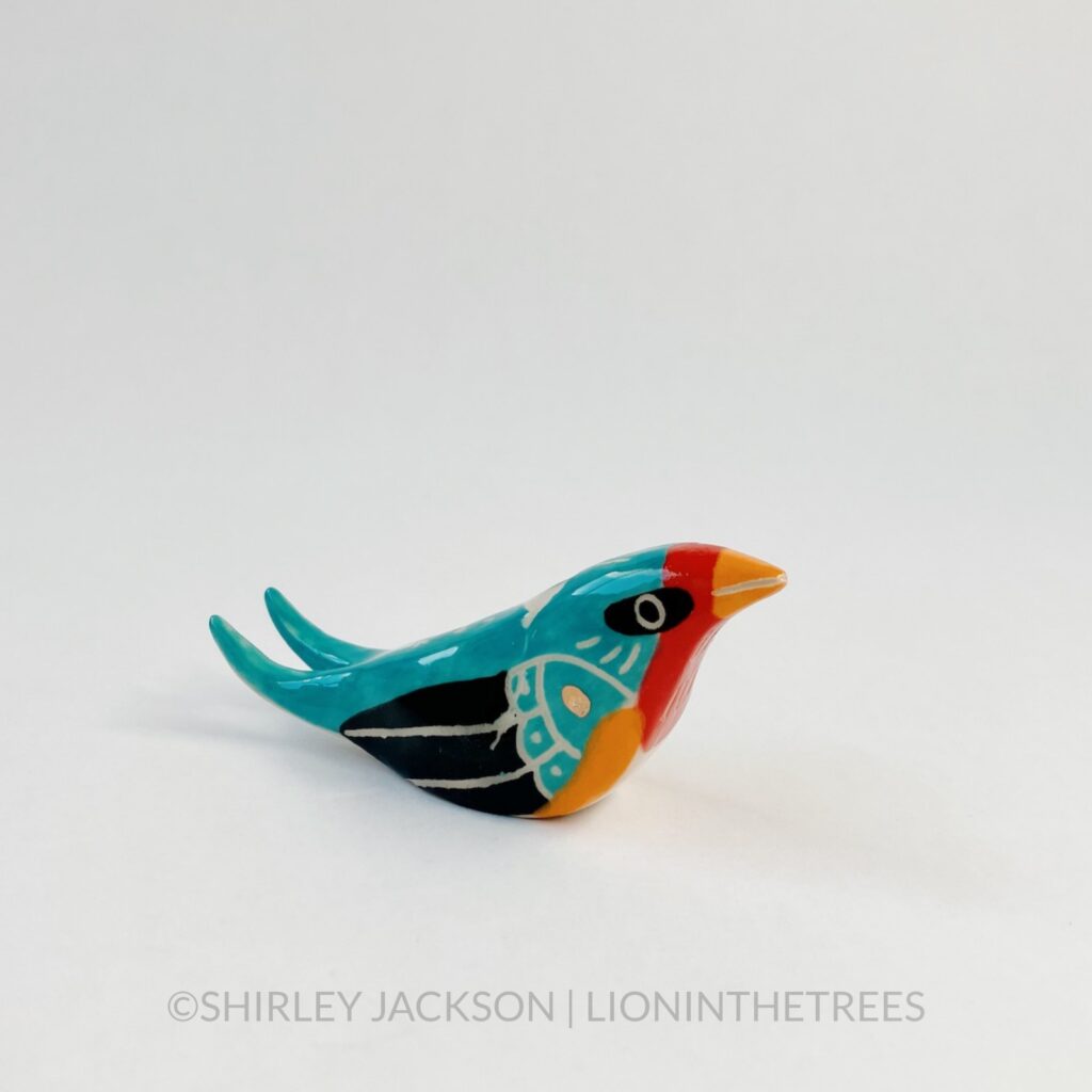 A small Barn Swallow totem done with turquoise, black, orange, and red underglazes. There are sgraffito details all over it’s body along with a small addition of gold glaze on it’s wings. Right side view.