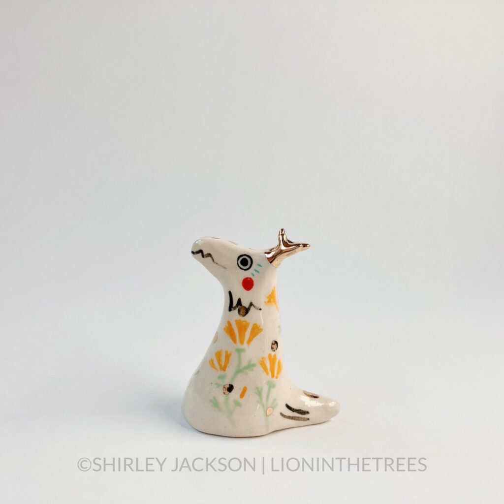 A small cream-white dragon totem decorated with details done with underglaze such as California Poppies and other markings.