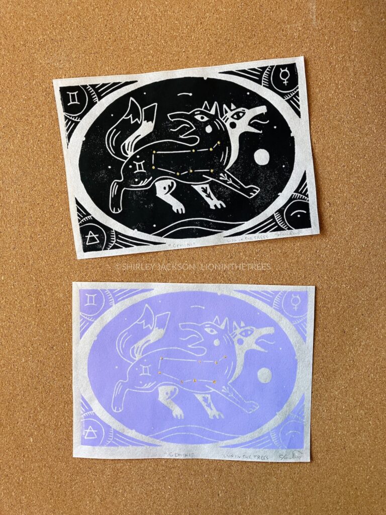 Photo showing two block prints of my two-headed fox Gemini design. The top print was done with black ink and the print on the bottom was done with the custom lilac ink.