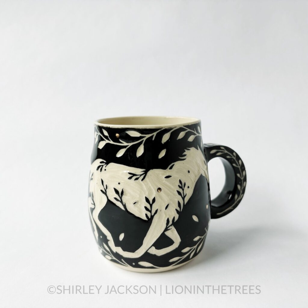 Ceramic black sgraffito mug featuring my Running Horse motif. This mug also features a floral border above and below the Horse motif.