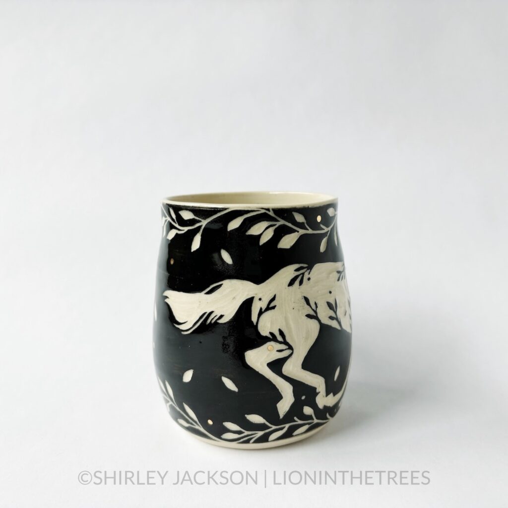 Ceramic black sgraffito mug featuring my Running Horse motif. This mug also features a floral border above and below the Horse motif.