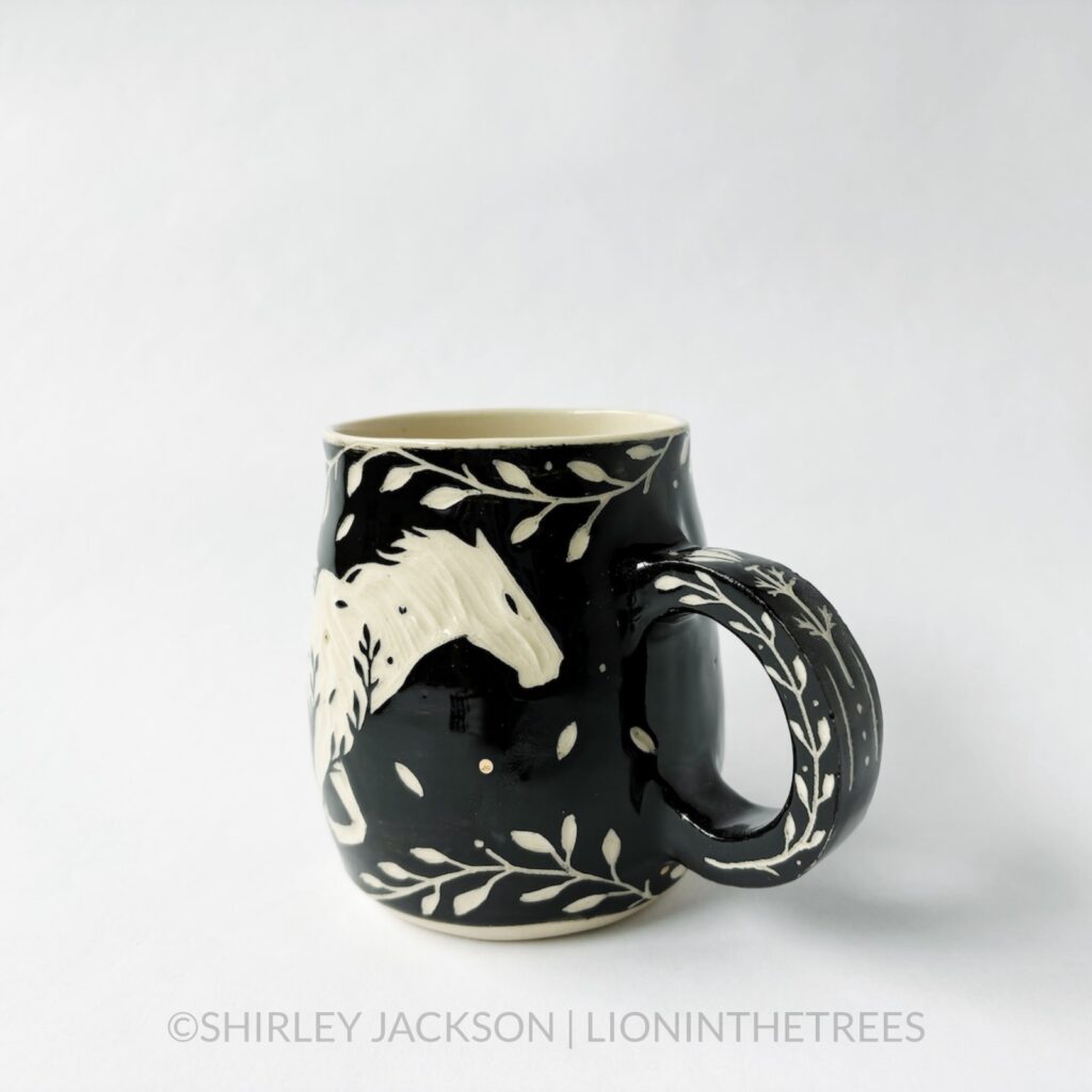 Ceramic black sgraffito mug featuring my Running Horse motif. This mug also features a floral border above and below the Horse motif.