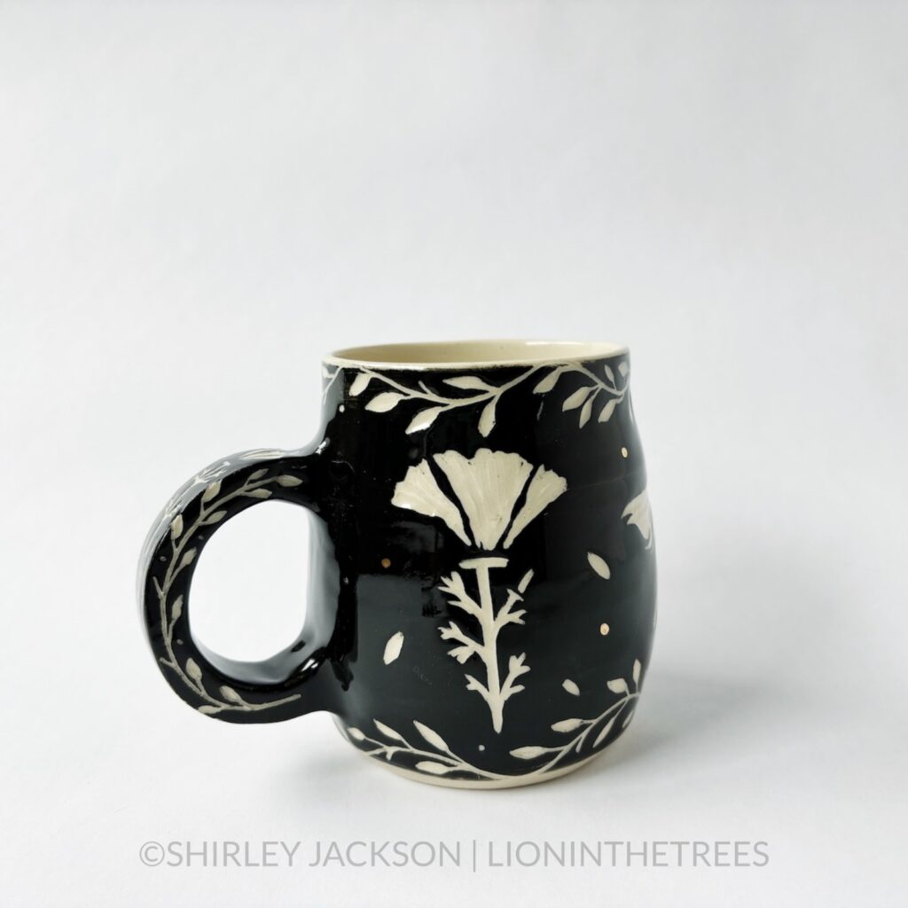 Ceramic black sgraffito mug featuring my Running Horse motif. This mug also features a floral border above and below the Horse motif.